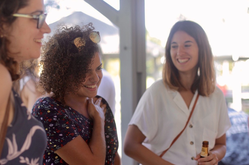 dos chicas sonriendo entre ellas. Una lleva un vestido de flores y la otra una camisa blanca